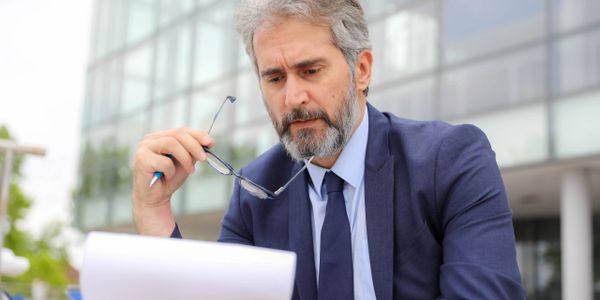 A focused businessman reviewing documents outdoors near a modern building.