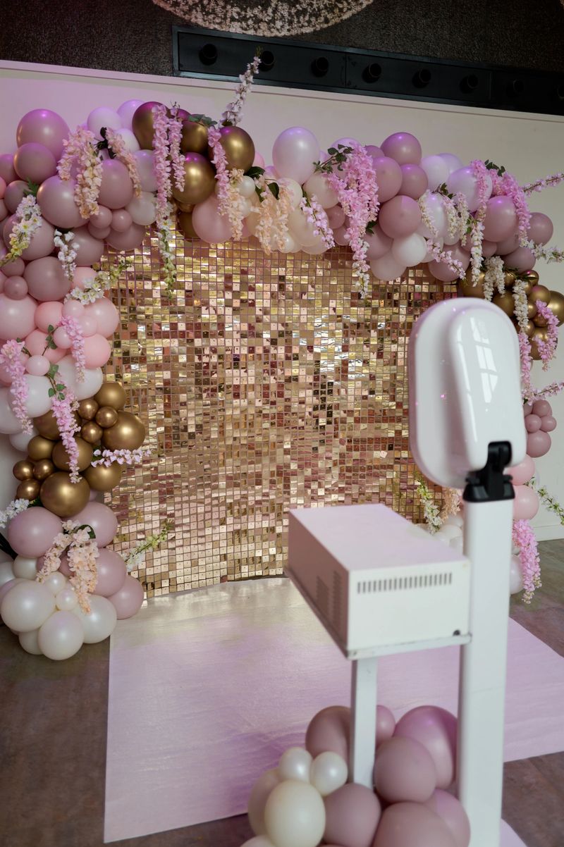 Modern photo booth setup featuring a gold sequin backdrop, adorned with pink and gold balloons, ready to capture memories at a special event