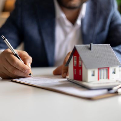 Person signing a document beside a miniature house model on a table.