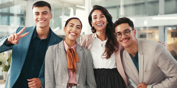 Four diverse professionals smiling together in a modern office setting.