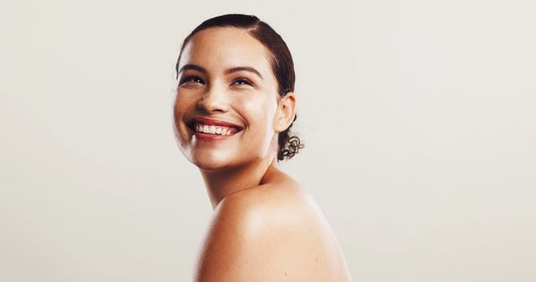 A woman with smooth skin smiling brightly against a light background.