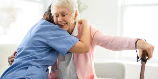 Elderly woman with a walking cane hugging a caregiver.