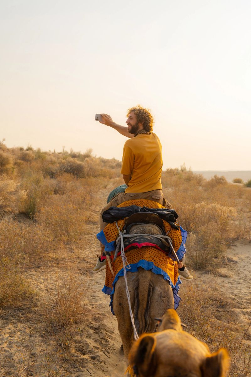 Man photographing with smartphone riding on camel through the desert in Jaisalmer, India