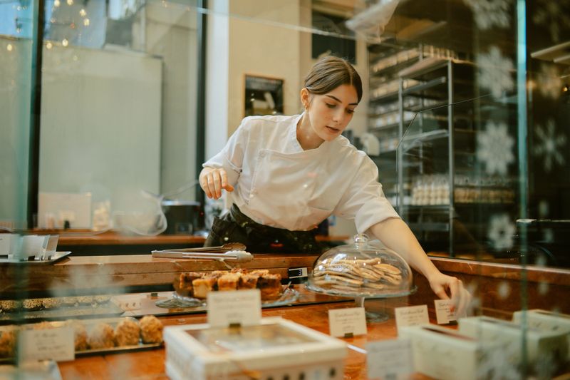 Young woman, a small business owner, working in a lovely French bakery in Tokyo, Japan. She is arranging cakes, loving her work in a chic patisserie.
