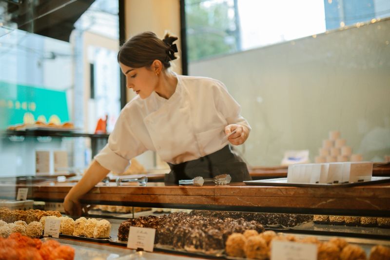 Young woman, a small business owner, working in a lovely French bakery in Tokyo, Japan. She is arranging cakes, loving her work in a chic patisserie.