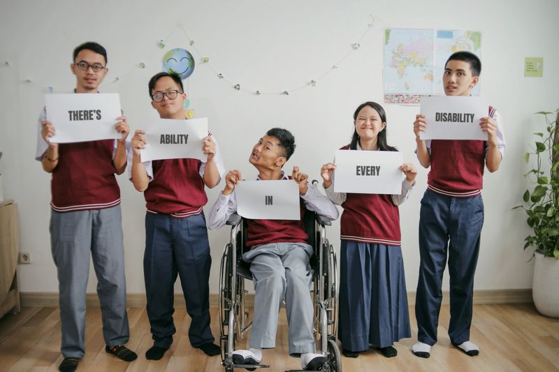 Portrait Of Group Students With Disabilities Showing Motivation Quotes On Paper With Text There's Ability in Every Disability.
