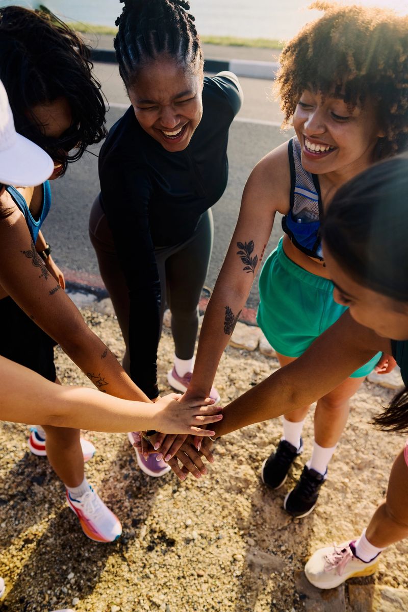 Four young female runners are getting ready for their run, stacking hands and smiling at each other