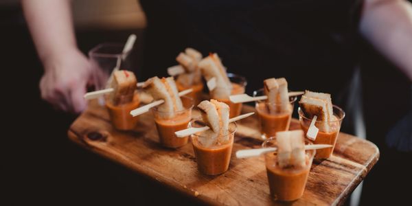 Small glasses of soup with bread pieces on a wooden tray.