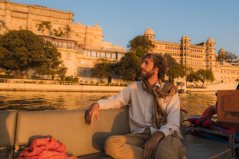 Man traveling by boat on Pichola lake and looking at Udaipur cityscape
