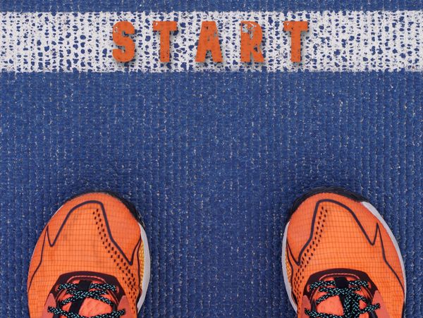 Runner wearing orange shoes at the starting line on a blue track.