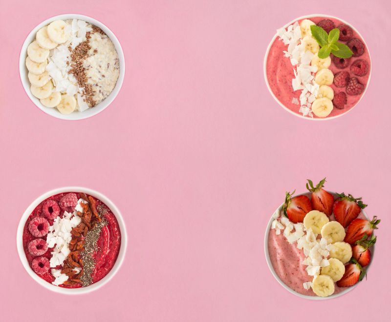 Smoothie with berries, fruits and oatmeal in the white bowls on a pink background. Top view. Copy space.