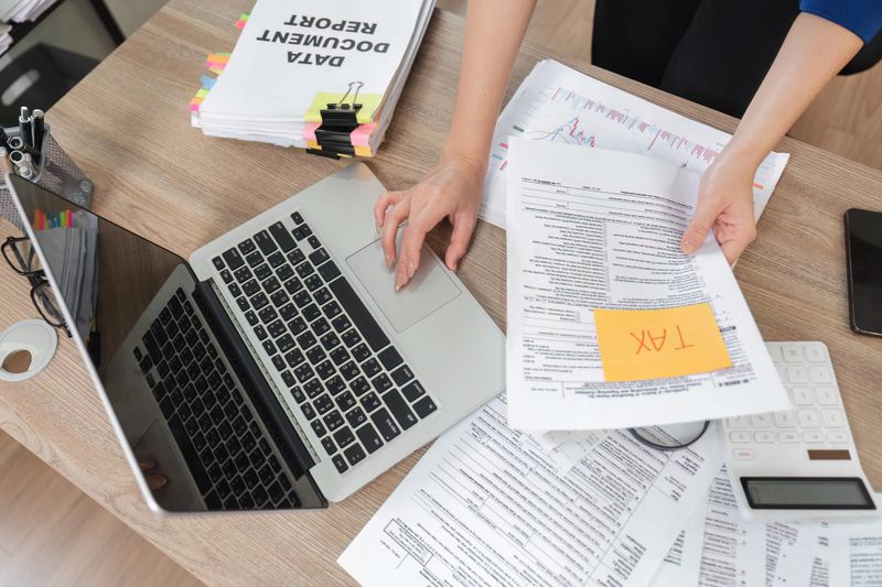 A focused businesswoman reviews tax paperwork while working on her laptop, showcasing her financial expertise.