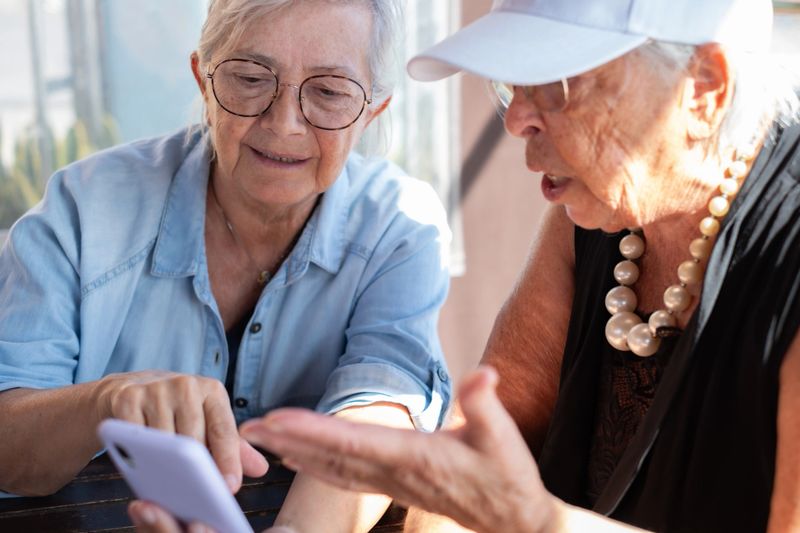 Two elderly women joyfully sharing a moment looking at a smartphone together. Their expressions convey happiness, friendship, positivity and companionship, staying connected in the digital age