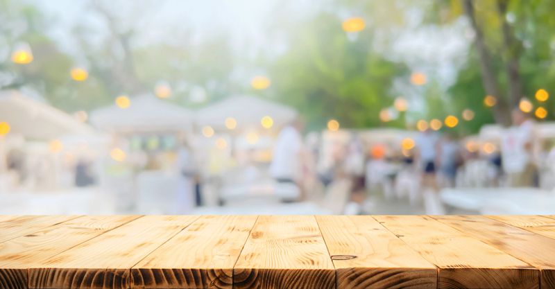 Rustic wooden table in the foreground with a blurred background of an outdoor market or garden party.ideal for displaying food, drinks, or products.not ai generated
