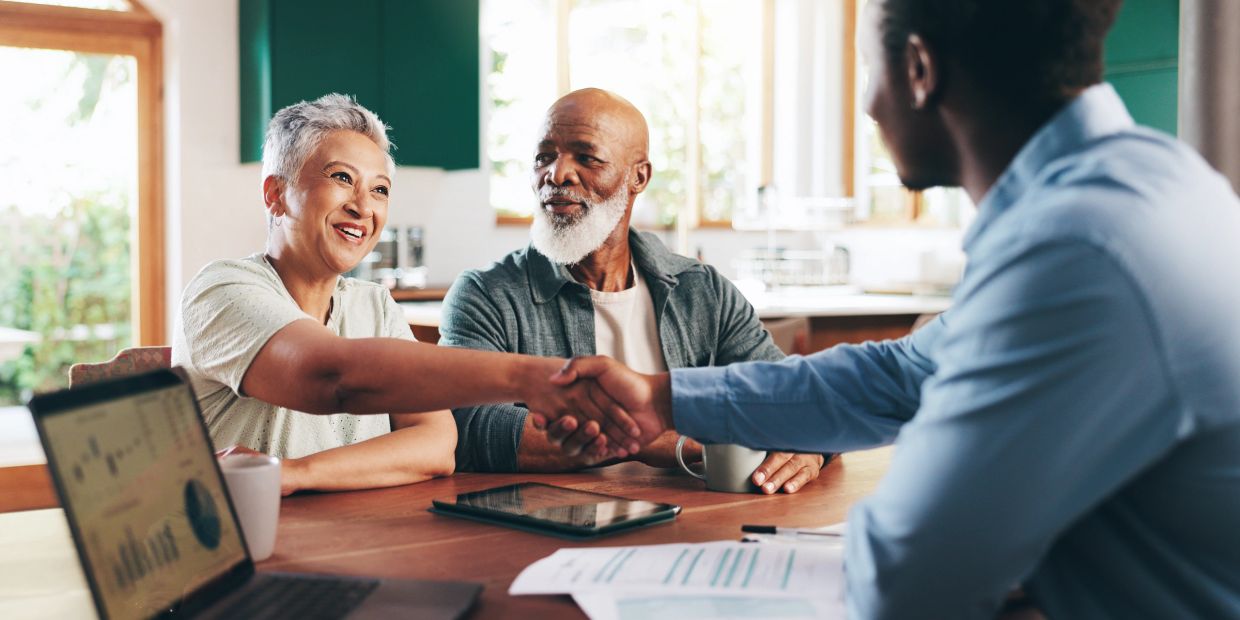 Senior couple shaking hands with a financial advisor in a cozy home setting.