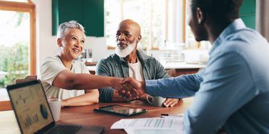 A couple shaking hands with a professional in a bright office.