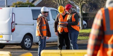 Tres trabajadores de construcción con cascos y chalecos naranjas.