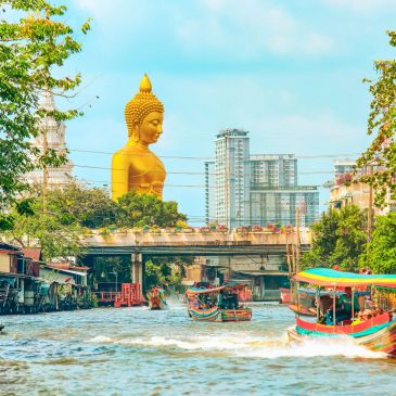 A large golden Buddha statue overlooking a bustling river with boats and buildings.