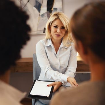 Woman in a professional setting speaking to two people with a clipboard.