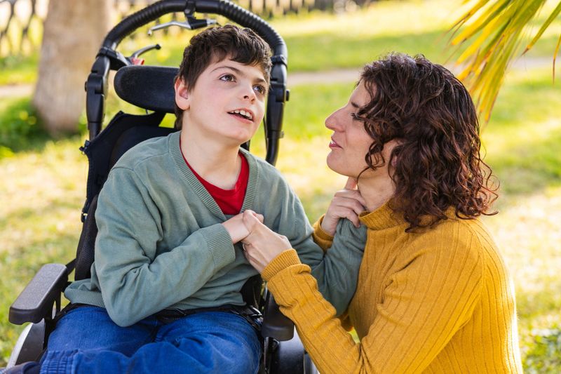 Mother interacting with her son with disability in a wheelchair, in a park, demonstrating love and care