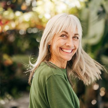 Smiling mature woman with gray hair outdoors in green shirt.