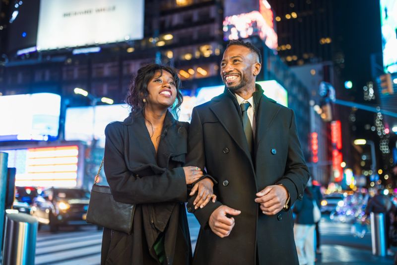 Elegantly dressed couple walking towards theatre in Times Square, Manhattan, NYC during the evening.