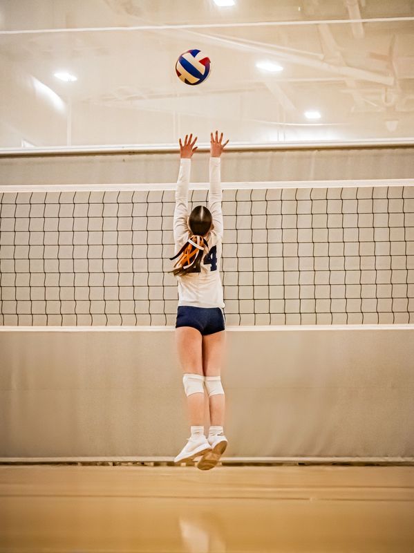 A volleyball player jumps to block the ball above the net.