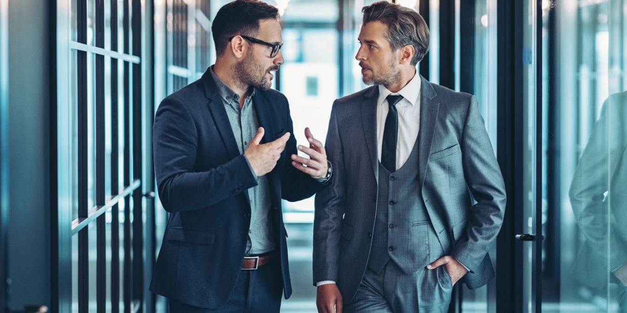 Dos hombres de negocios conversando en un pasillo moderno.