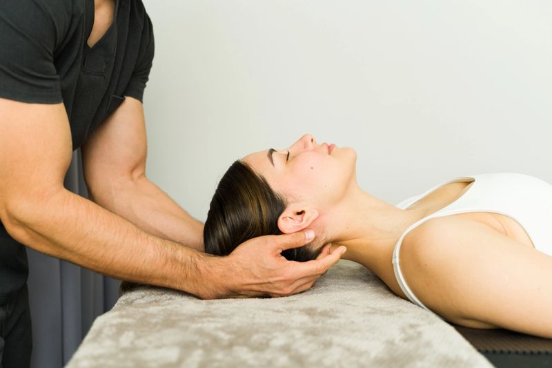 Professional physiotherapist performing neck massage on a young woman lying on a massage table, providing relief from pain and tension