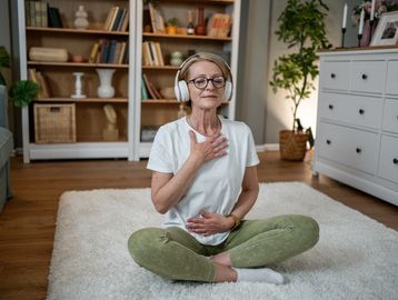 Elderly woman practicing mindful breathing with headphones in cozy living room.