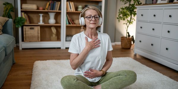 Elderly woman meditating with headphones indoors.