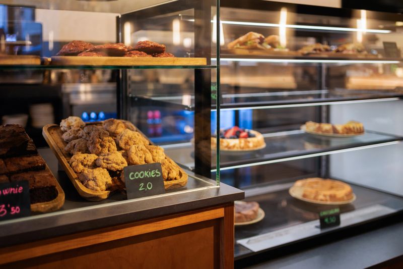 Delicious cookies, brownies, cakes, and sandwiches are displayed in a glass case at a cafe, ready to be enjoyed