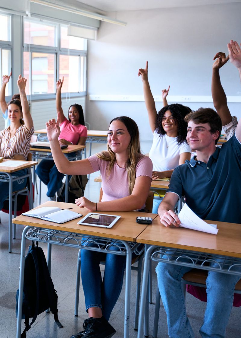 Vertical. Student in the classroom raising her hand to ask a question during class. High school student asks the teacher a question. Selective focus. High quality photo