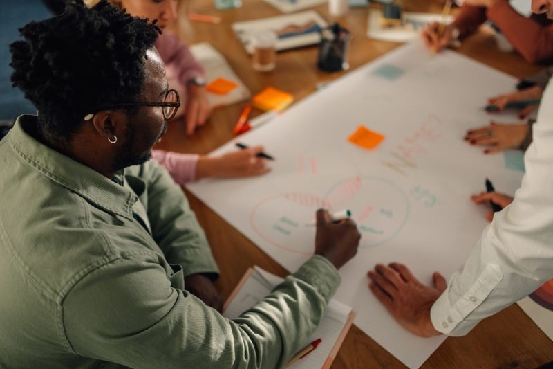 Marketing team members are collaborating on a venn diagram during a brainstorming session, working together to visualize and analyze data for effective marketing strategies