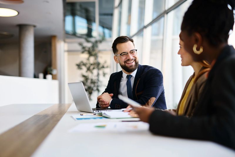 Two business partners engaging in a strategic discussion within a modern office, collaborating over a laptop while analyzing important documents together during their meeting