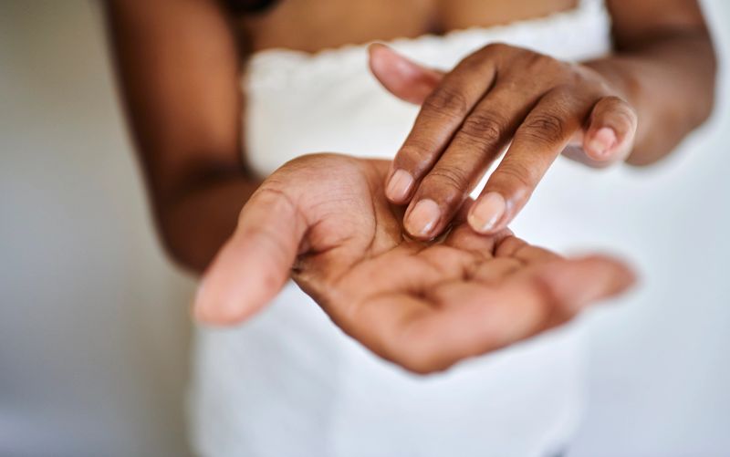 Close-up of a woman with medium-toned skin applying skincare oil to her hands. The image emphasizes self-care, hydration, and soft, well-nourished skin.
