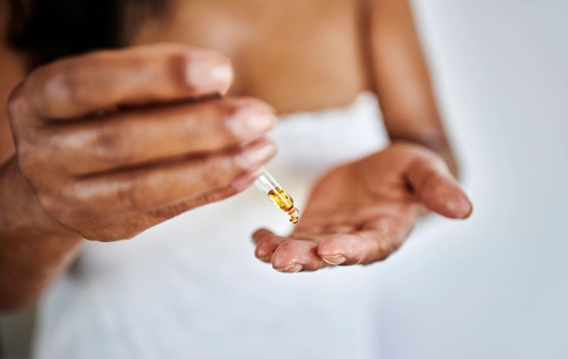 A close-up of a woman with medium skin tone applying an organic skincare serum with a dropper onto her hand, emphasizing self-care and beauty.
