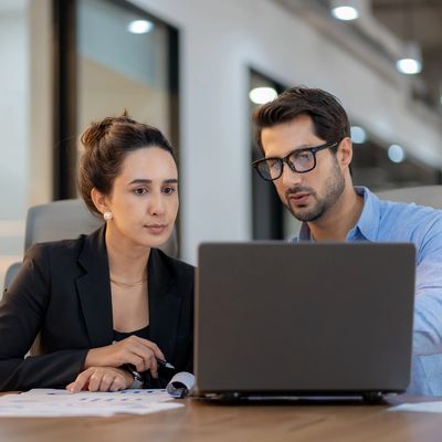 Two professionals discussing work while looking at a laptop in an office.