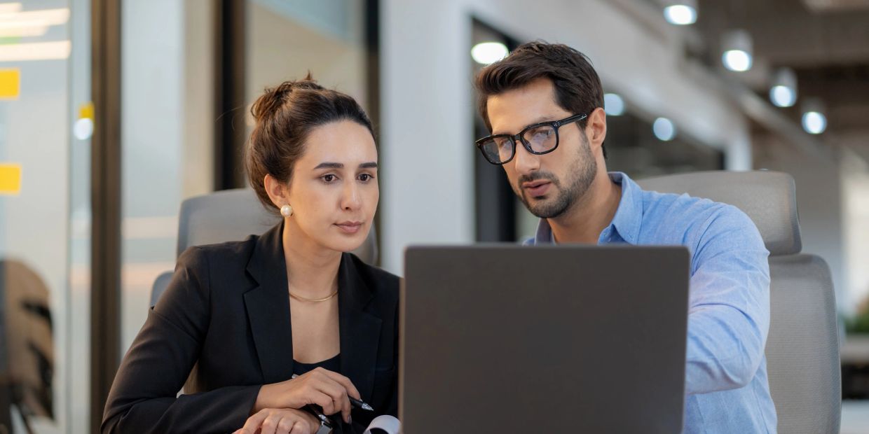 Dos personas trabajando juntas frente a una computadora portátil.
