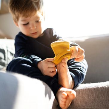 Child putting on yellow sock indoors.