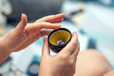 Person scooping balm from a small jar with fingers.