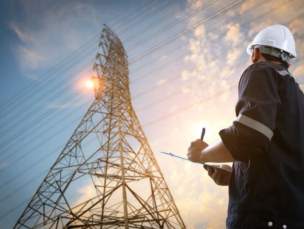 Engineer inspecting power lines near a transmission tower at sunset.