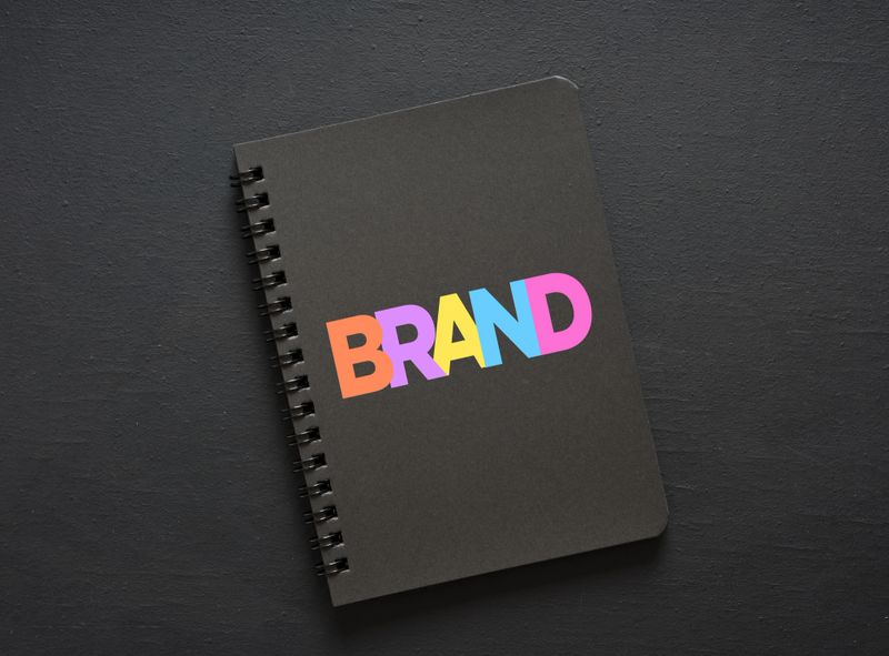 Colorful letters composing the word brand on a black notebook placed on a dark surface, representing branding strategy