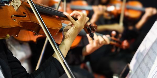 Close-up of violinists playing in an orchestra with sheet music in view.