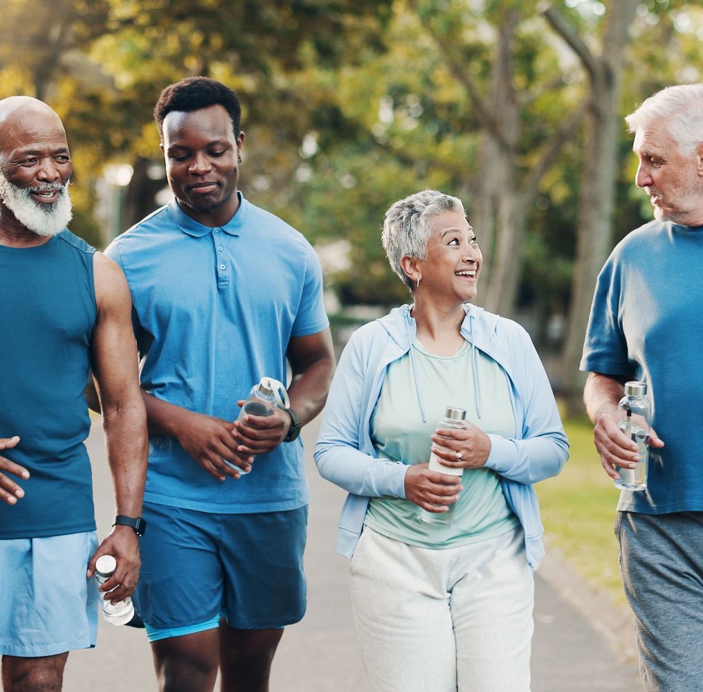 Group of diverse adults walking in the park, holding water bottles and chatting joyfully.