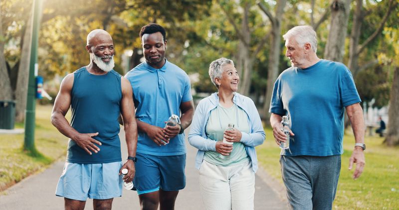 People, talking and walking for fitness outdoor of mobility training, discussion and morning routine. Senior, community and coach with conversation, exercise and motivation for cardio workout at park
