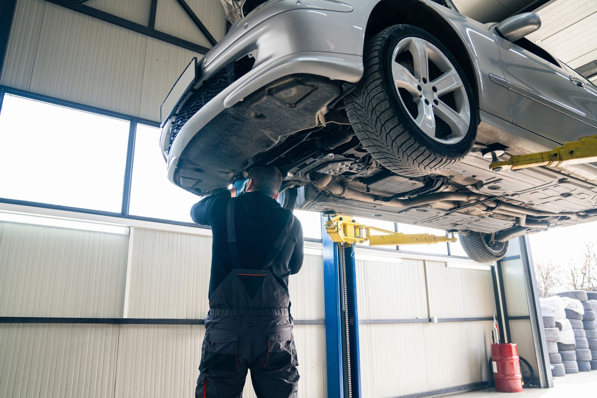Mechanic inspecting car's underside on a lift in a garage.