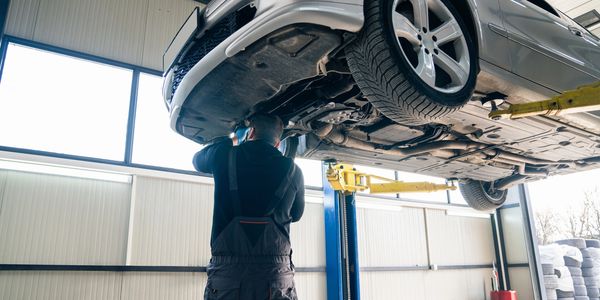 Mechanic inspecting car underside on lift in garage.