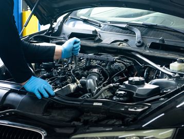 Mechanic repairing a car engine wearing blue gloves.