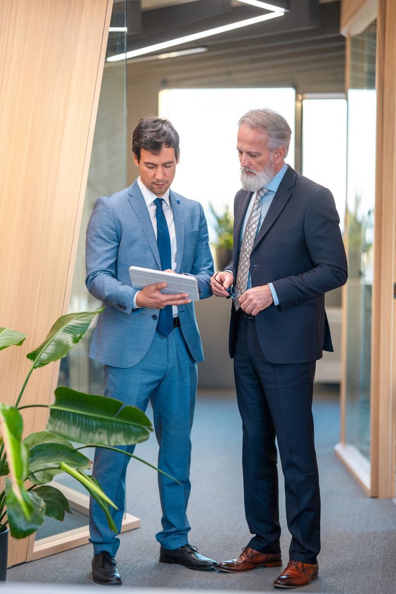 A mature Caucasian man and a mid-adult Asian man, both stock brokers in professional attire, engaged in financial discussions in a modern office setting.